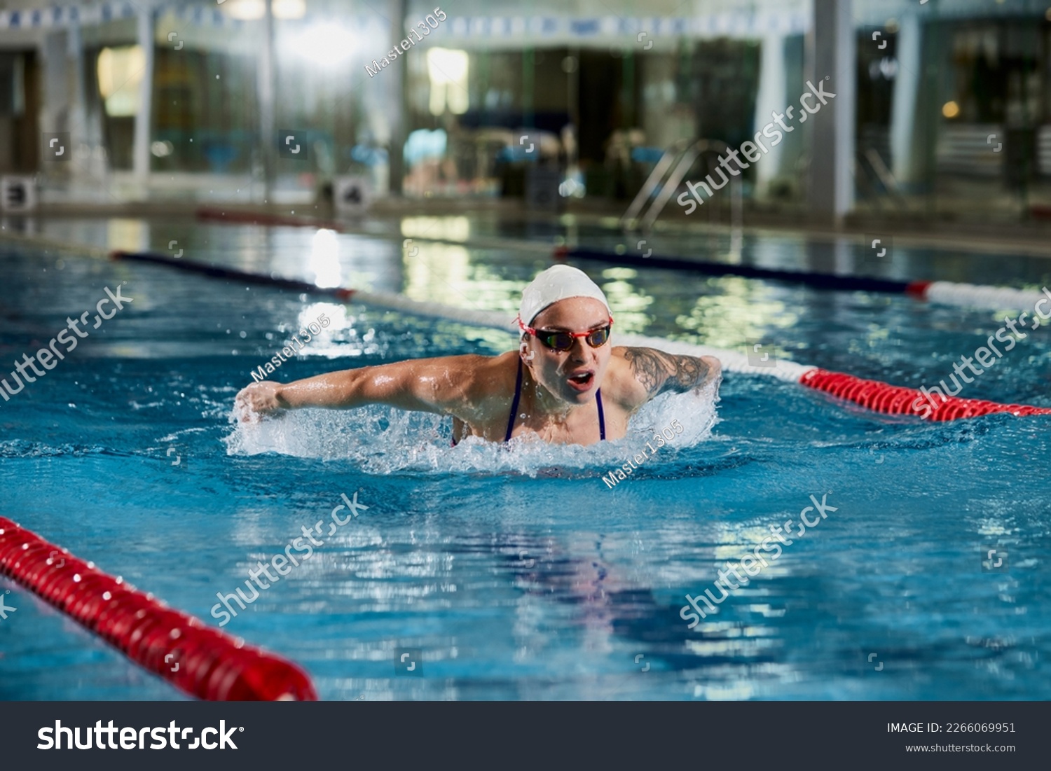 Butterfly swimming type. Young woman, professional female swimming athlete in cap and goggles training in pool indoors. Concept of sport, endurance, competition, energy, healthy lifestyle #2266069951