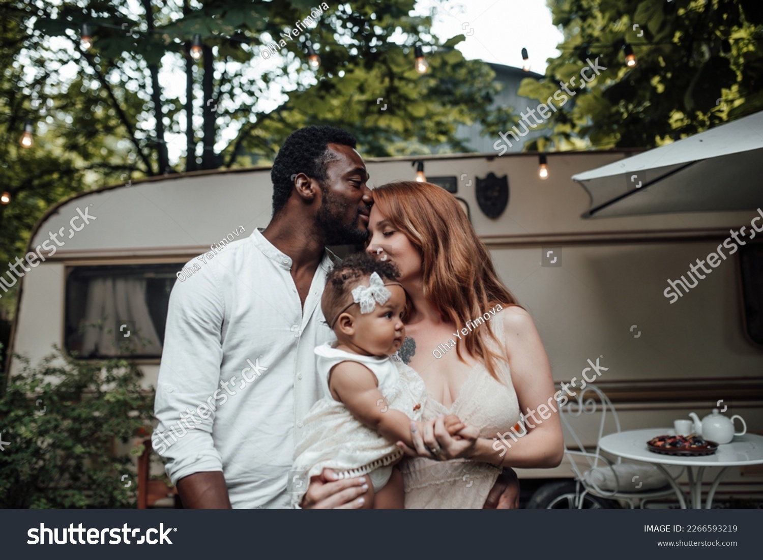 Mixed race family with dark skinned infant daughter spend time together hugs and kisses in camper park. African american man his fair skin wife and little girl enjoying summer vacation in open air #2266593219