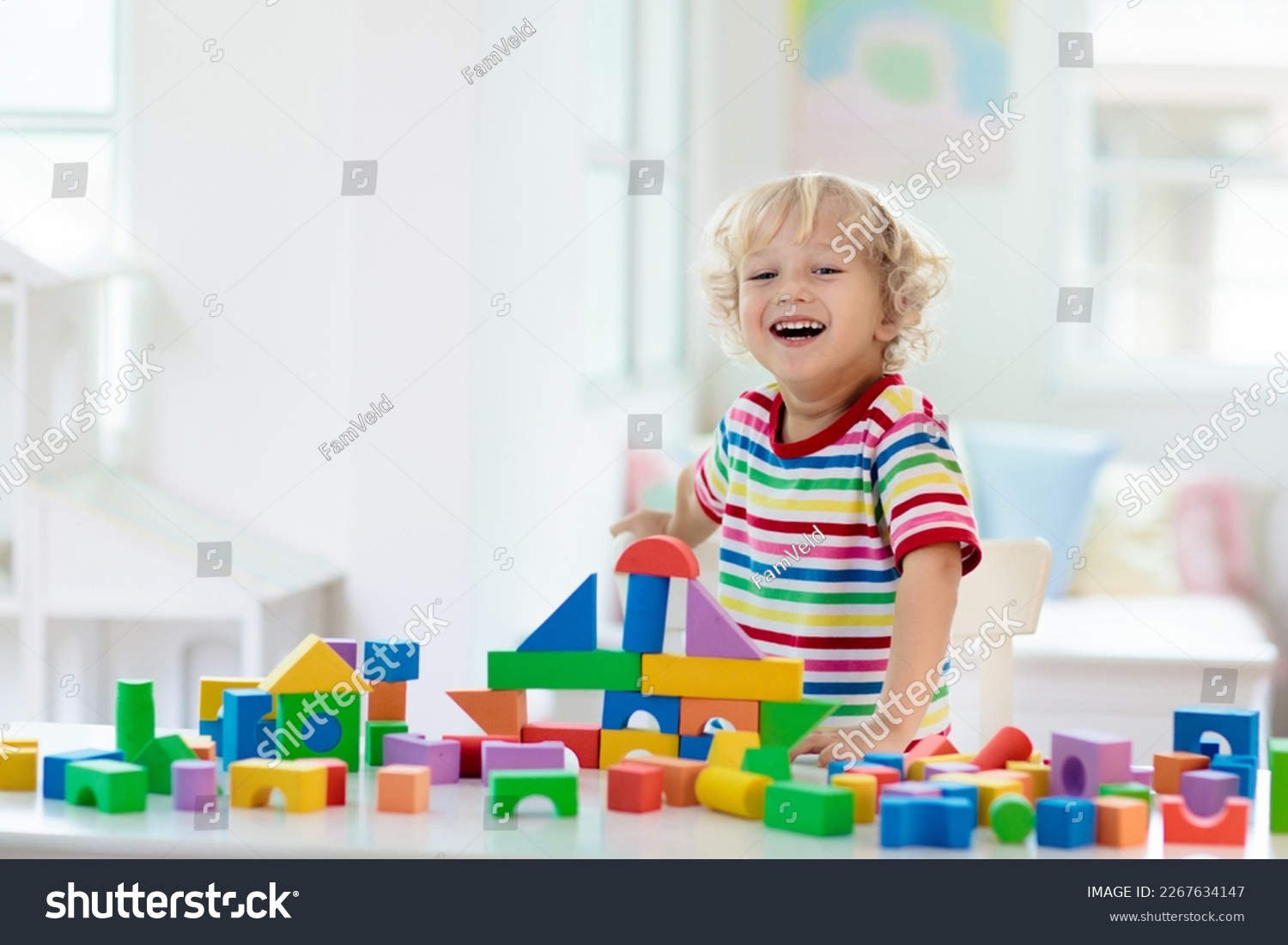Kid playing with colorful toy blocks. Little boy building tower of block toys. Educational and creative toys and games for young children. Baby in white bedroom with rainbow bricks. Child at home. #2267634147