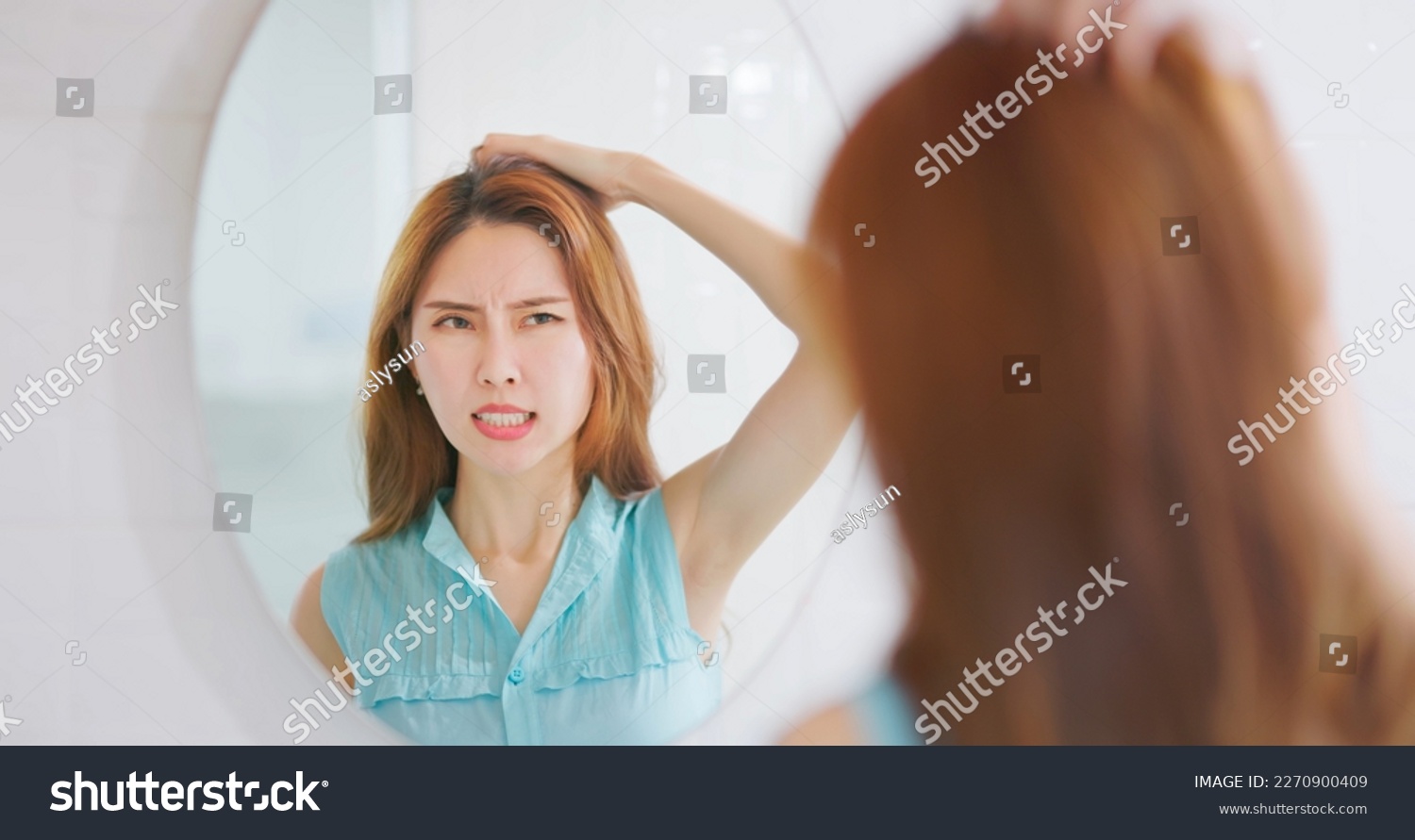 Asian woman looking in mirror is scratching head from itching and having messy oily hair #2270900409