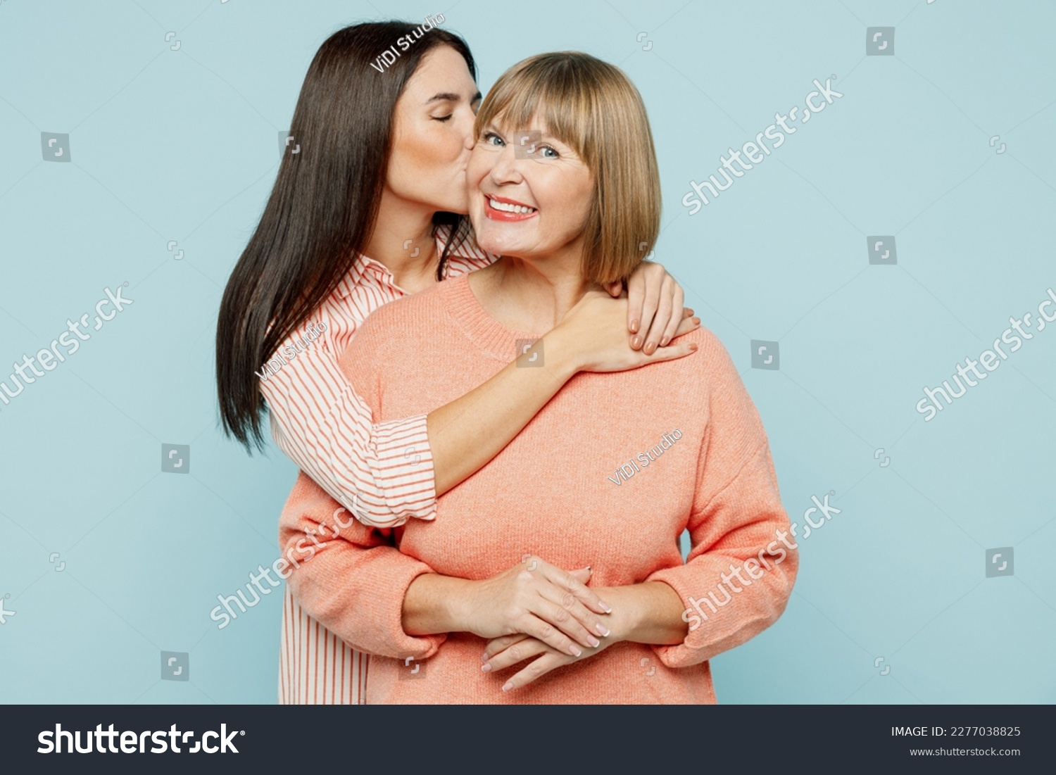 Lovely fun smiling happy caucasian elder parent mom with young adult daughter two women together wearing casual clothes hugging cuddle kiss isolated on plain blue cyan background. Family day concept #2277038825