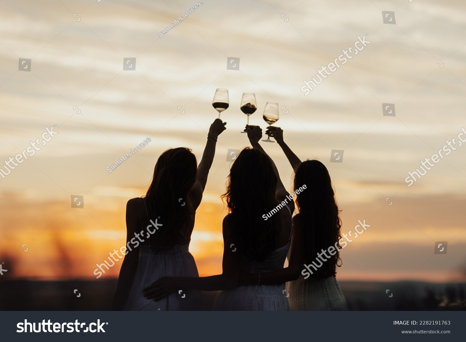 Silhouettes of women in the park in evening sunlight. The lights of a sun. The company of female friends enjoys a summer picnic and raise glasses with wine.  #2282191763