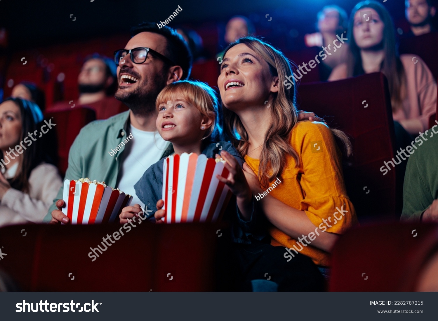 A young joyful couple is with their daughter in the cinema, watching an exciting movie. #2282787215