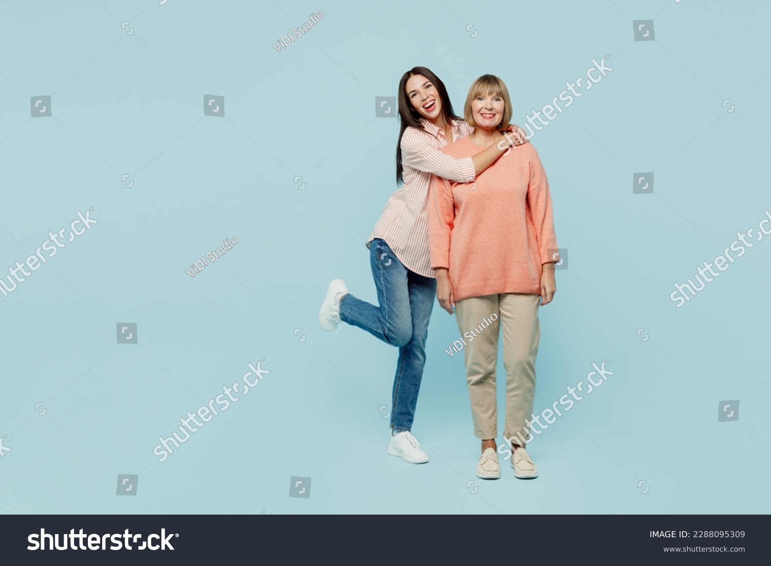 Full body smiling happy fun cheerful cool elder parent mom with young adult daughter two women together wear casual clothes look camera hugging isolated on plain blue background. Family day concept #2288095309