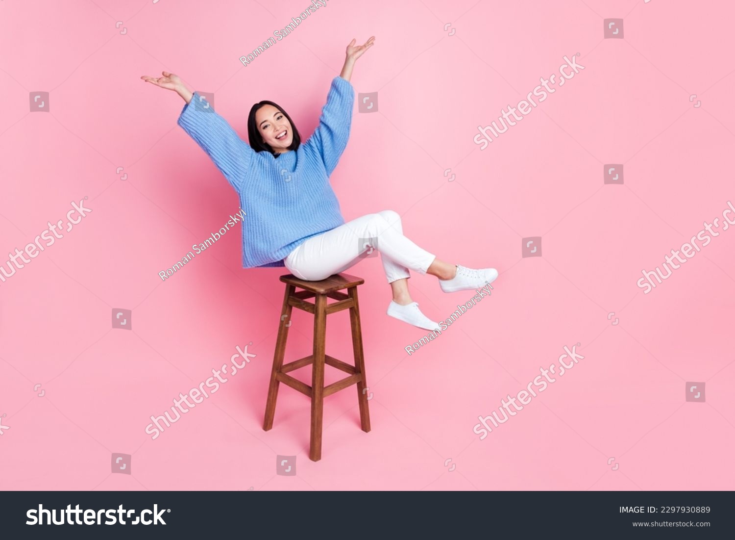 Full length photo of gorgeous pretty girl blue sweater white pants sitting on bar stool raising arms up isolated on pink color background #2297930889