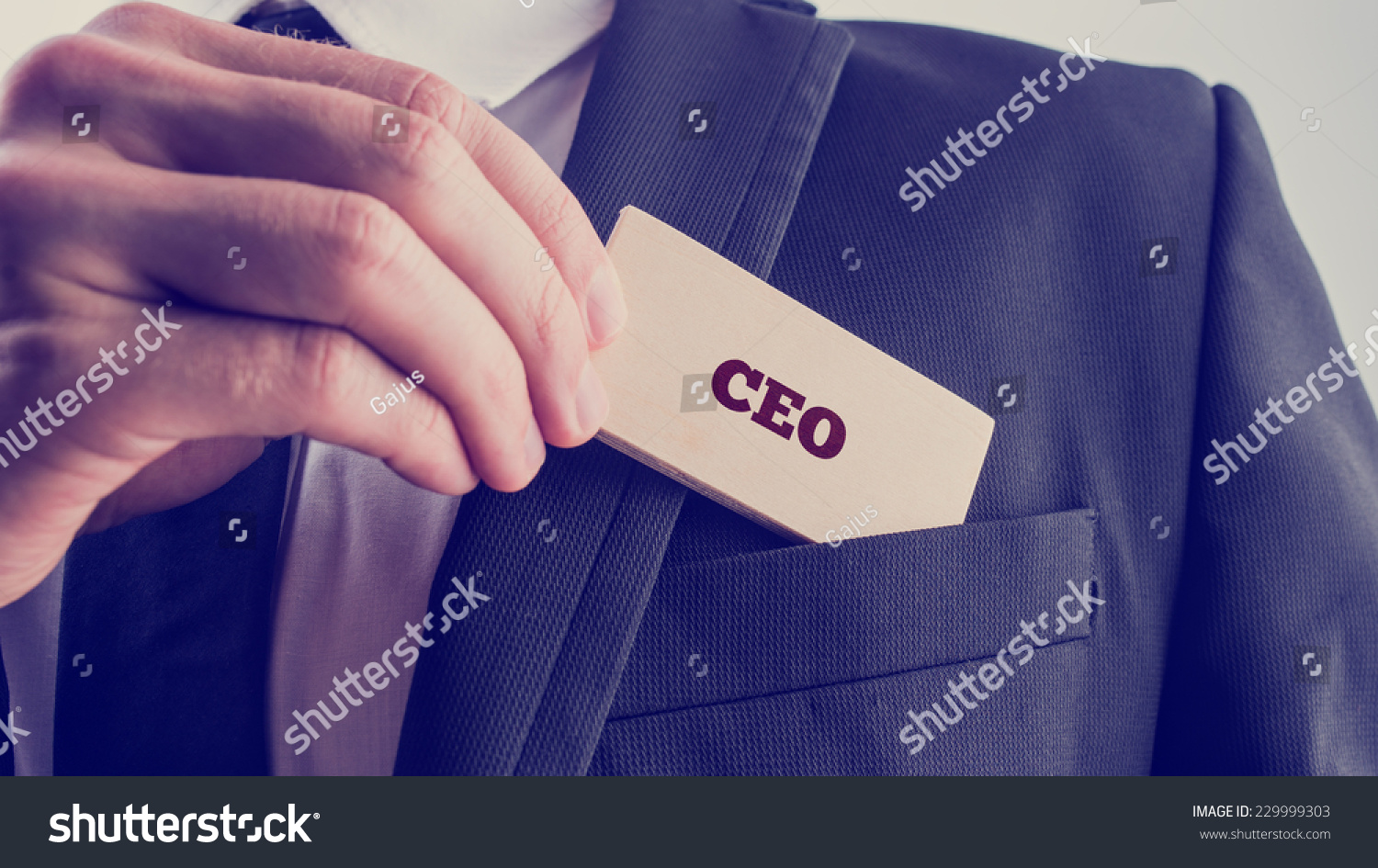 Retro style image of a businessman showing a wooden card reading - CEO - as he withdraws it from the pocket of his suit jacket. #229999303