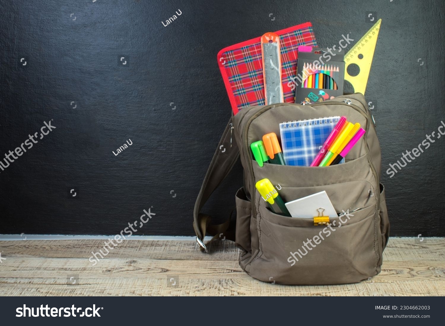 Backpack with different colorful stationery on table. Black background. Back to school #2304662003