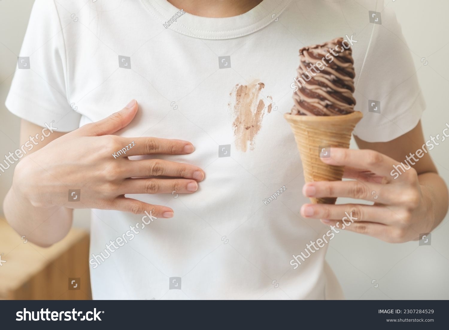 Cloth stain, disappointment asian young woman, girl eating melting ice cream in waffle cone on hot weather, hand show making chocolate cream drop on white t-shirt, spot dirty or smudge on clothes. #2307284529