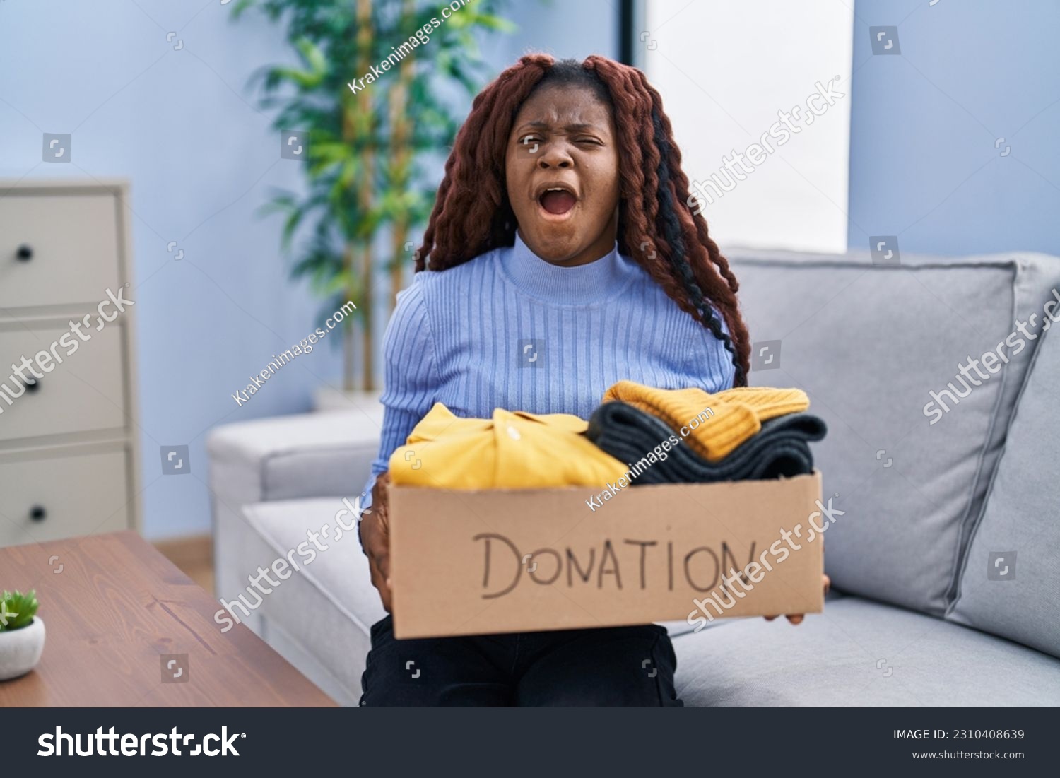 African woman holding donations box for charity angry and mad screaming frustrated and furious, shouting with anger looking up.  #2310408639