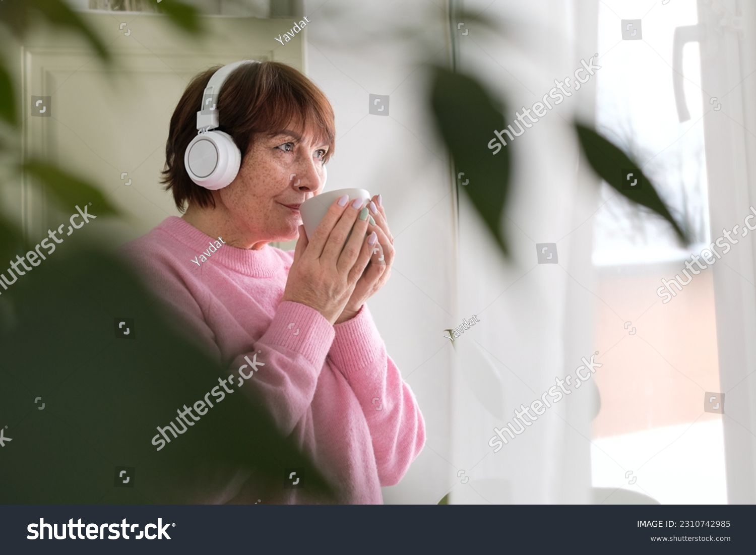 Elderly woman enjoying coffee music by the window. embracing modern life #2310742985