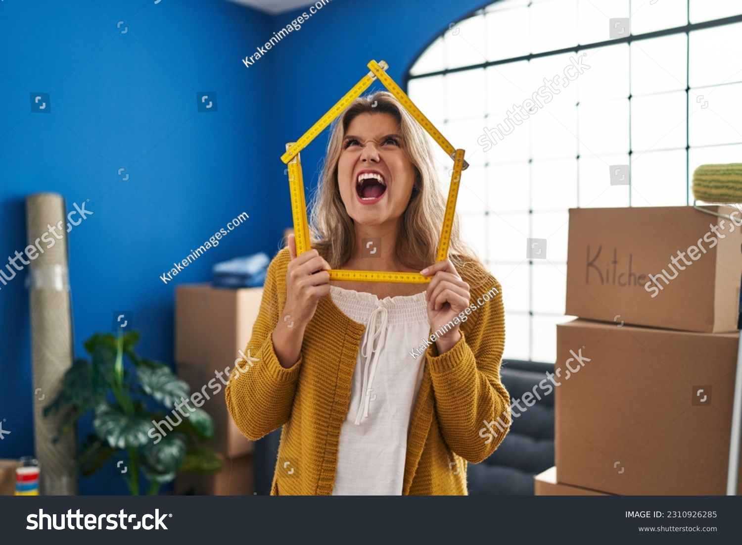 Young woman standing at new home angry and mad screaming frustrated and furious, shouting with anger looking up.  #2310926285