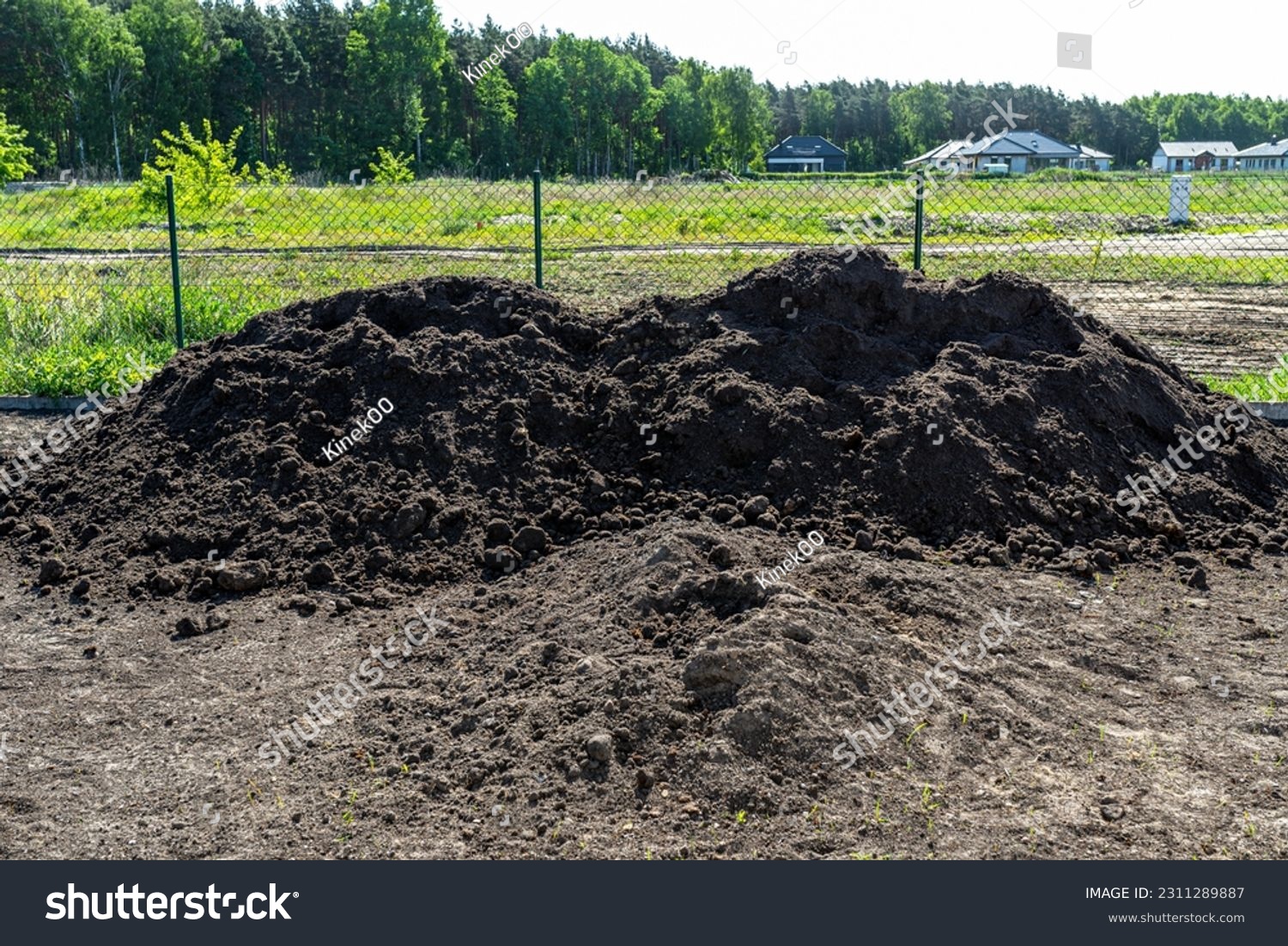 A heap of pure black earth lying in the yard next to the fence. #2311289887