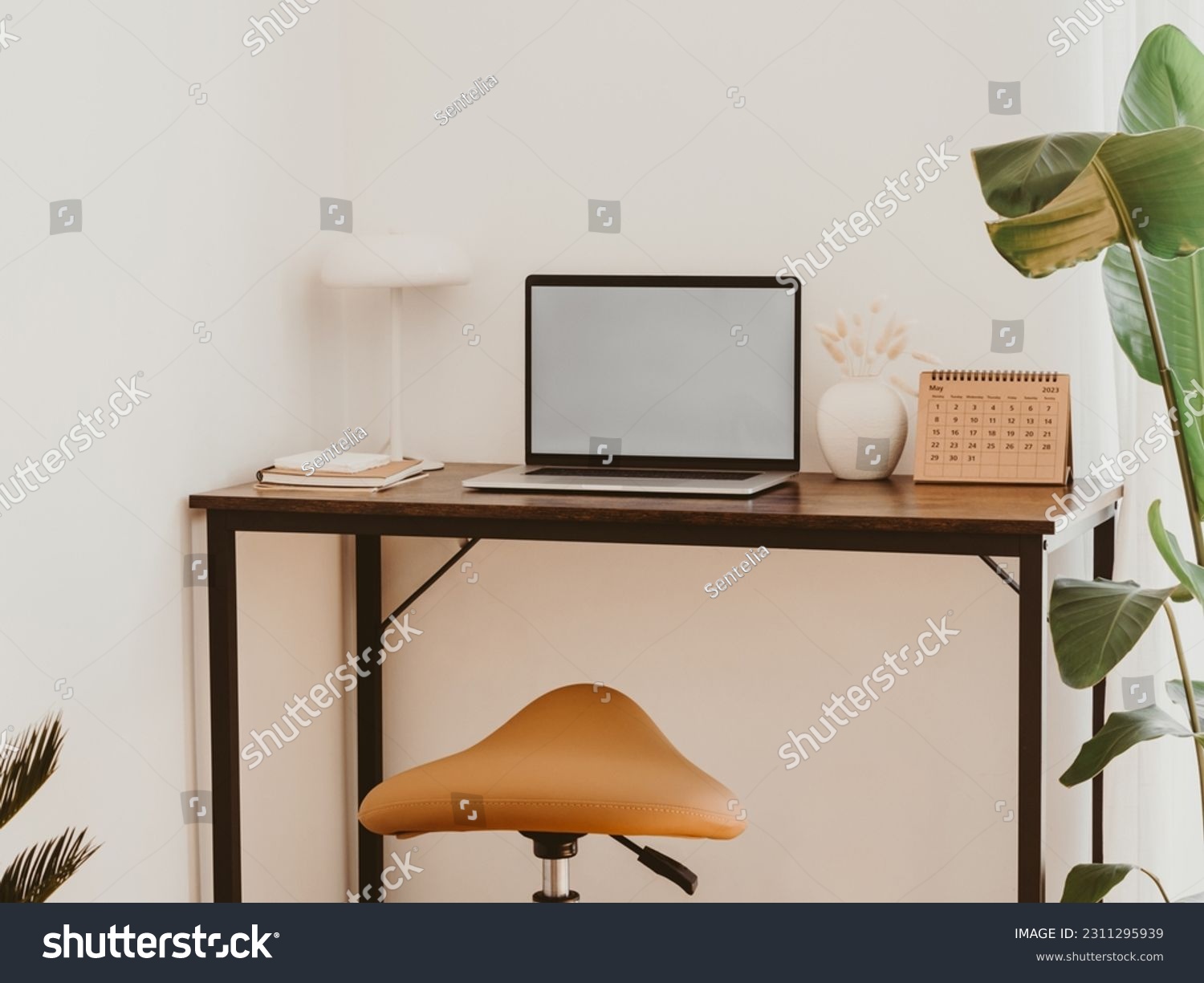 Stylish home office interior with laptop screen mockup, wooden table, plant, notes, saddle stool and elegant office accessories in designer apartment. #2311295939