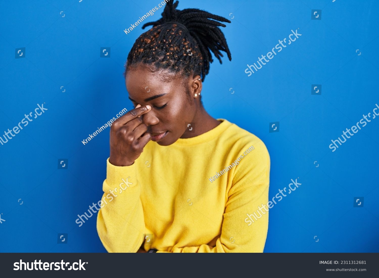 Beautiful black woman standing over blue background tired rubbing nose and eyes feeling fatigue and headache. stress and frustration concept.  #2311312681