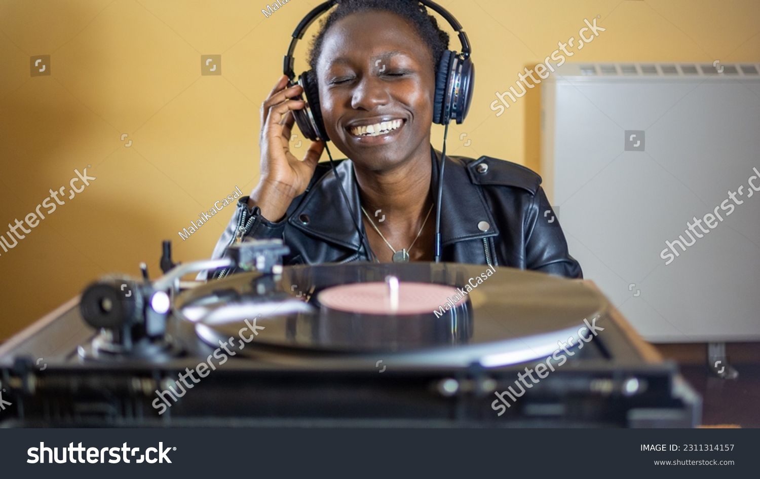 young woman wearing a leather jacket using headphones while playing a vinyl record on a vintage turntable #2311314157