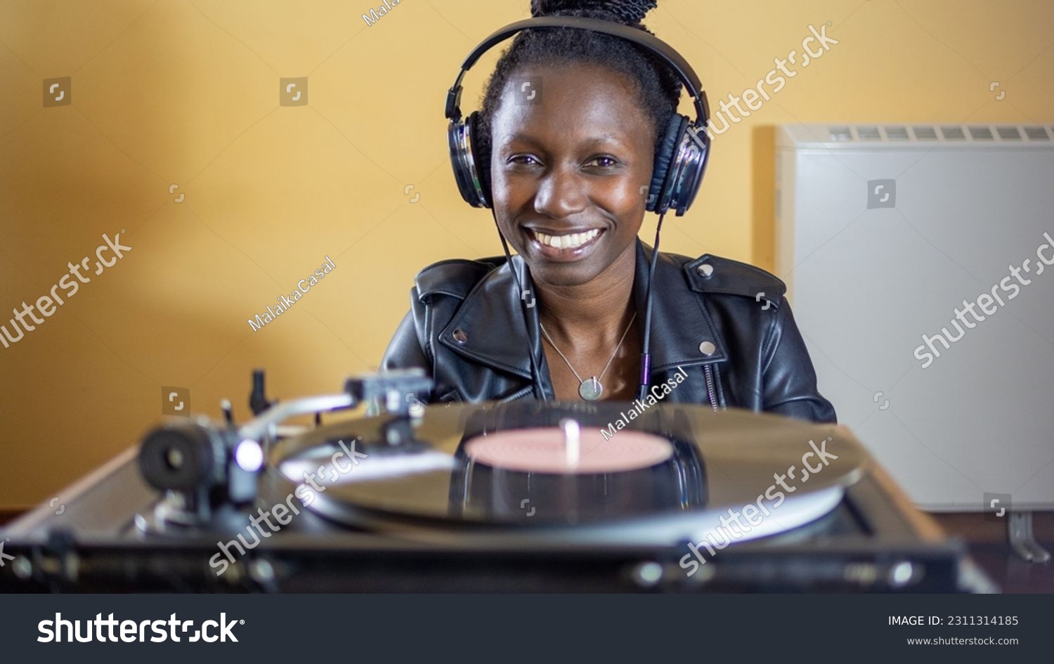 young woman wearing a leather jacket using headphones while playing a vinyl record on a vintage turntable #2311314185