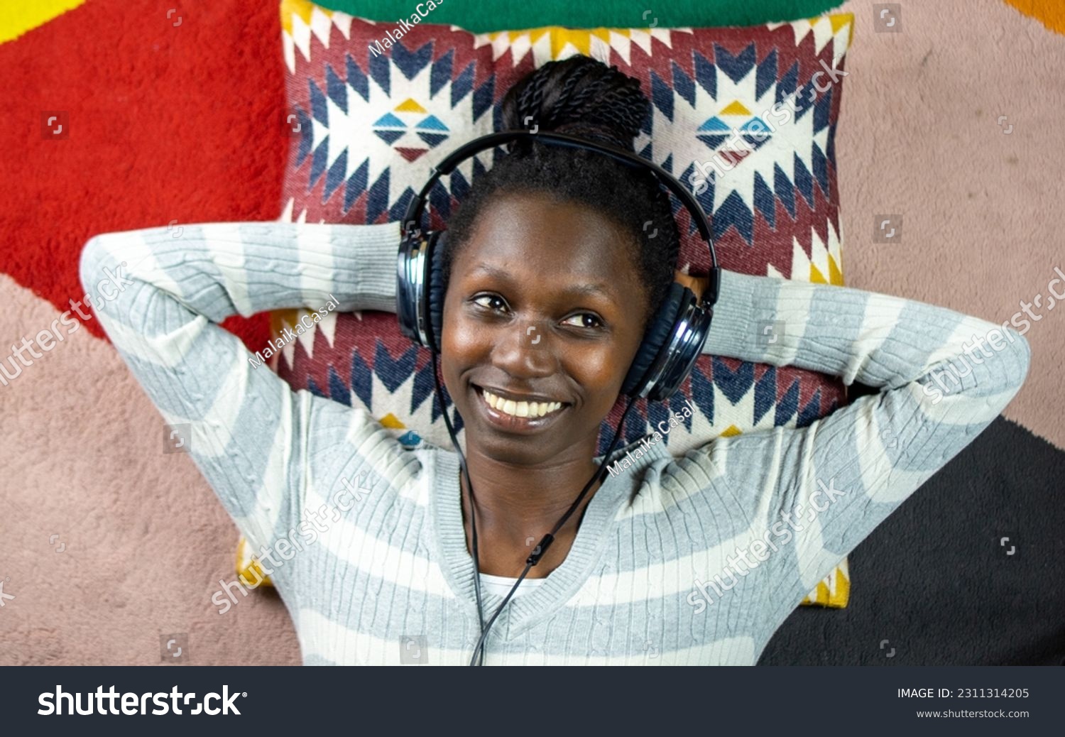 young woman using headphones while lying on a colorful carpet  #2311314205
