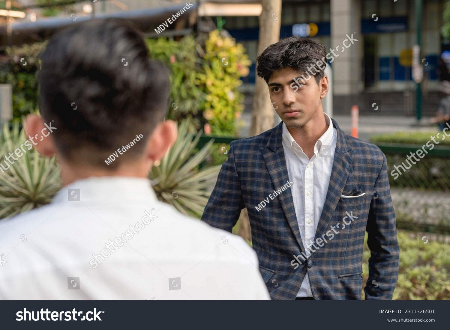 A hotheaded young indian man stares down his workmate while outside the office. Animosity in the workplace. #2311326501