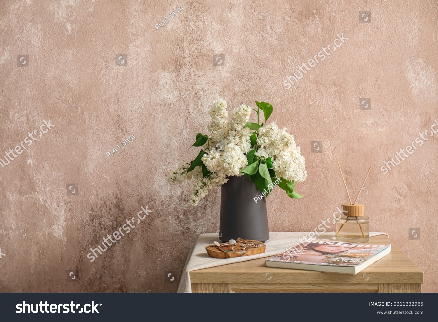 Vase with lilac flowers, jewelry, magazine and reed diffuser on table in room #2311332965