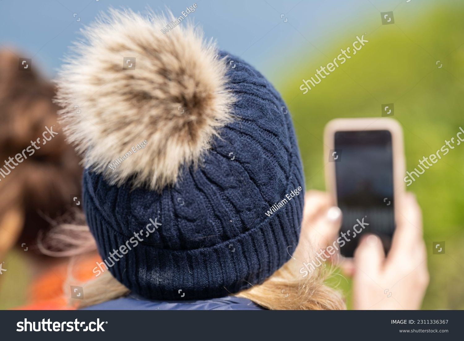 Old lady taking a photo on her phone, wearing a beanie. #2311336367