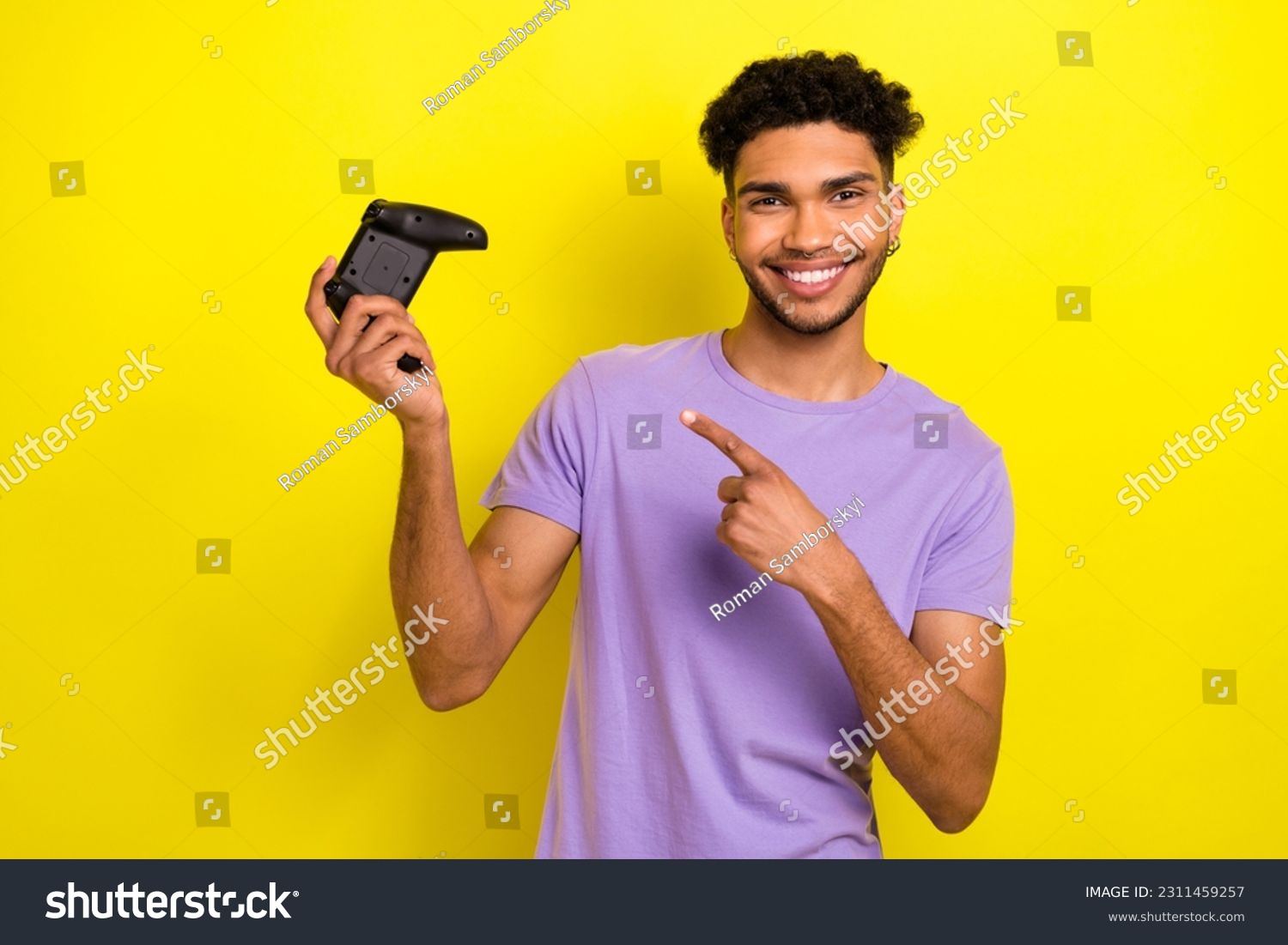 Portrait of handsome cheerful man indicate finger arm hold demonstrate controller isolated on yellow color background #2311459257