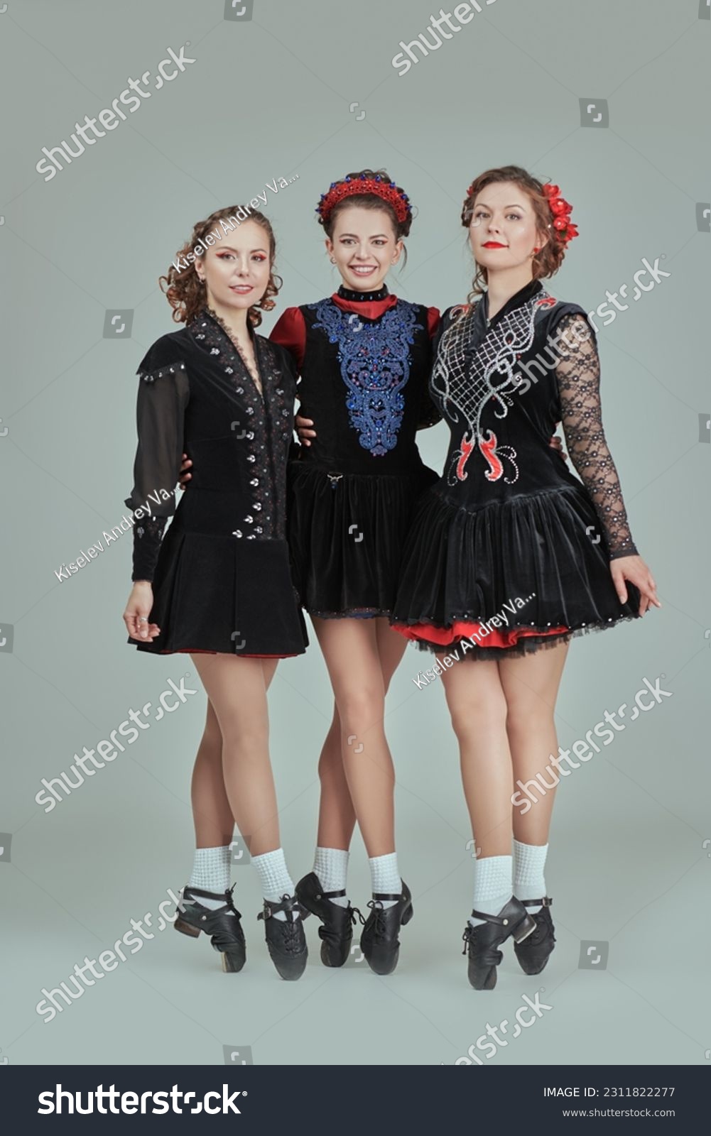 Professional women's Irish dance ensemble in concert costumes and Ghillies Hard Shoes pose together in a row. Full-length studio portrait on a grey background. #2311822277