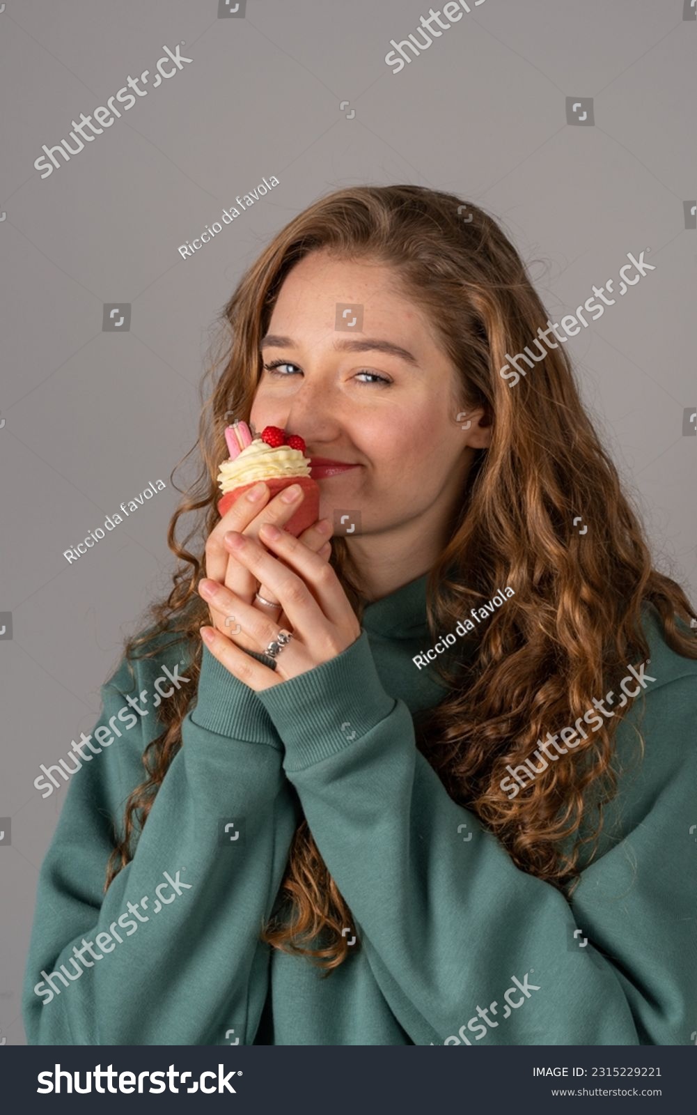 A cute girl is holding a cake-candle. Red-haired happy girl on a gray background #2315229221