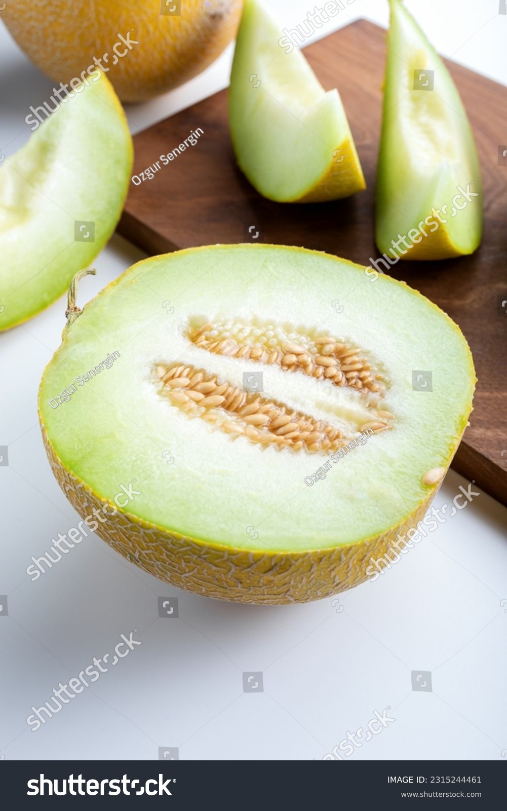 Half melon and sliced pieces of melon on wooden cutting board . #2315244461
