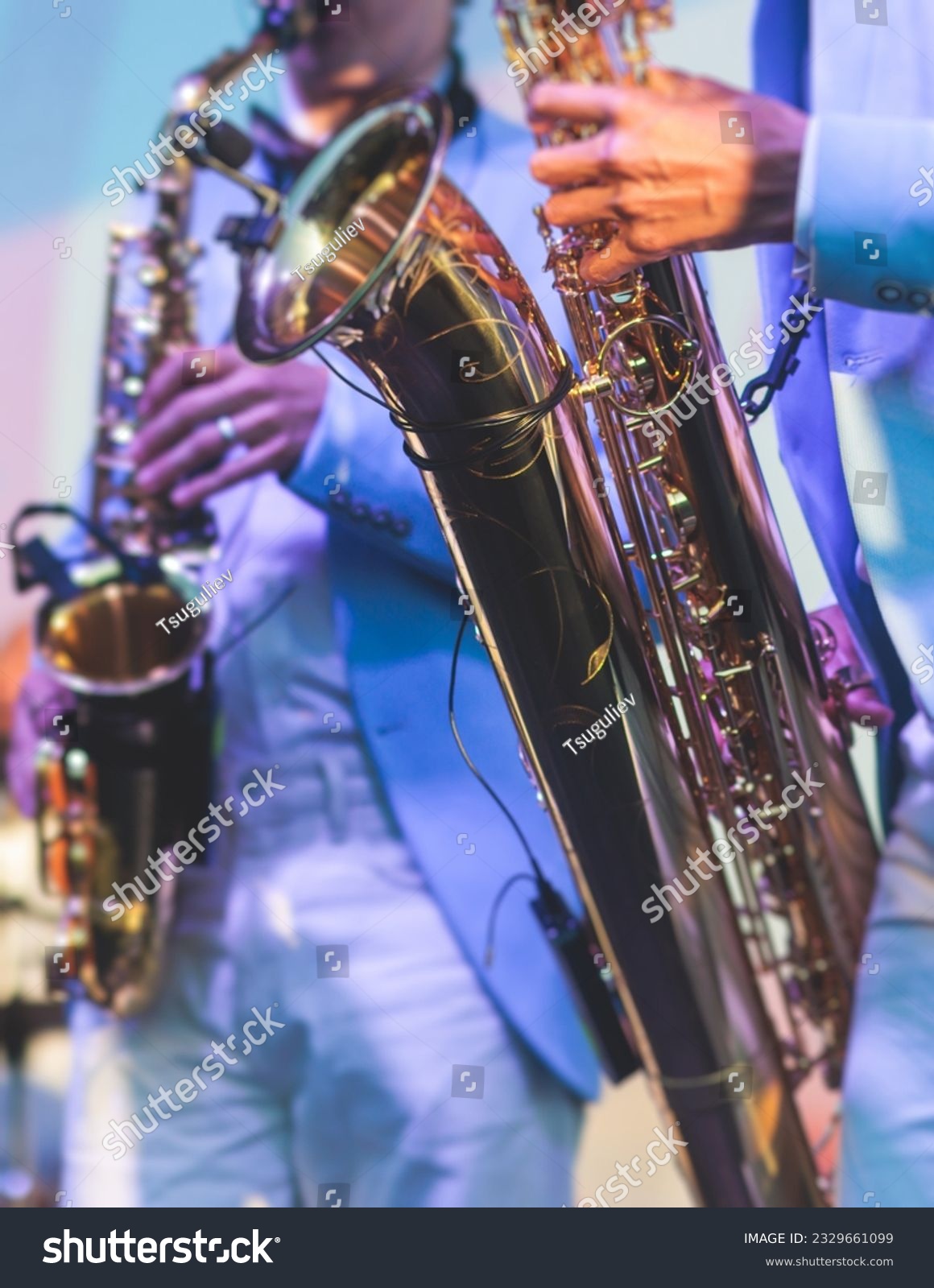 Concert view of saxophonist in a blue and white suit, a saxophone sax player with vocalist and musical band during jazz orchestra show performing music on stage in the scene lights #2329661099