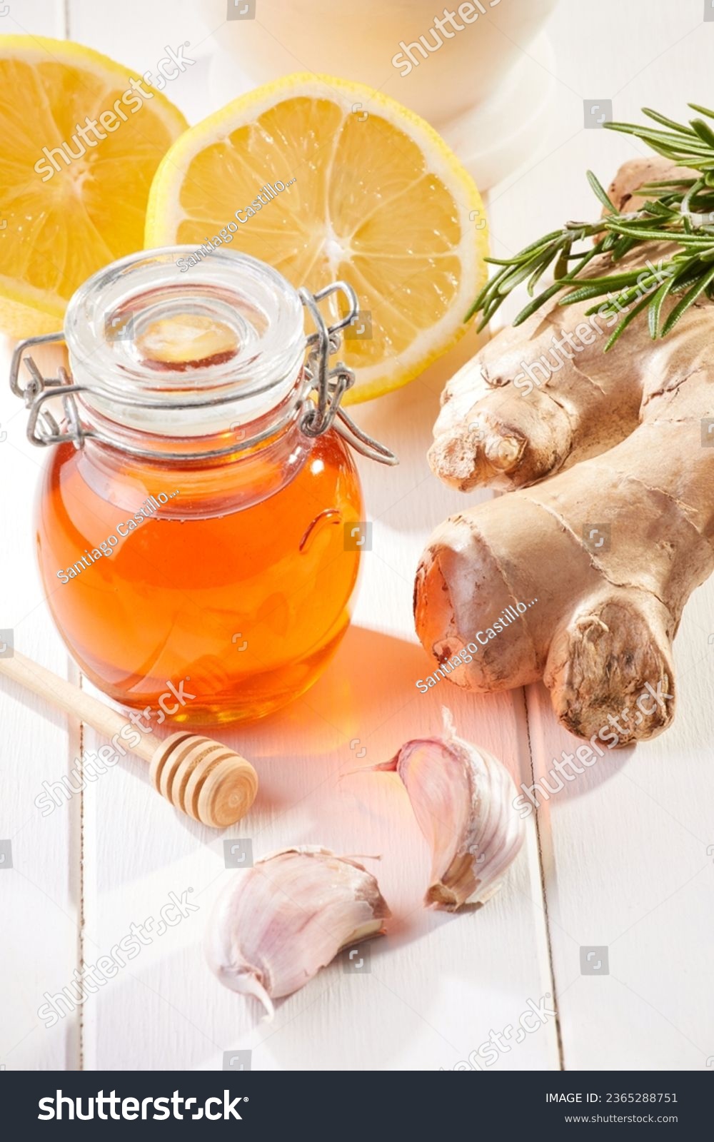 Jar of honey by some ginger, a clove of garlic, rosemary leaves and a sliced yellow lemon over a white wooden table. Natural remedies. #2365288751