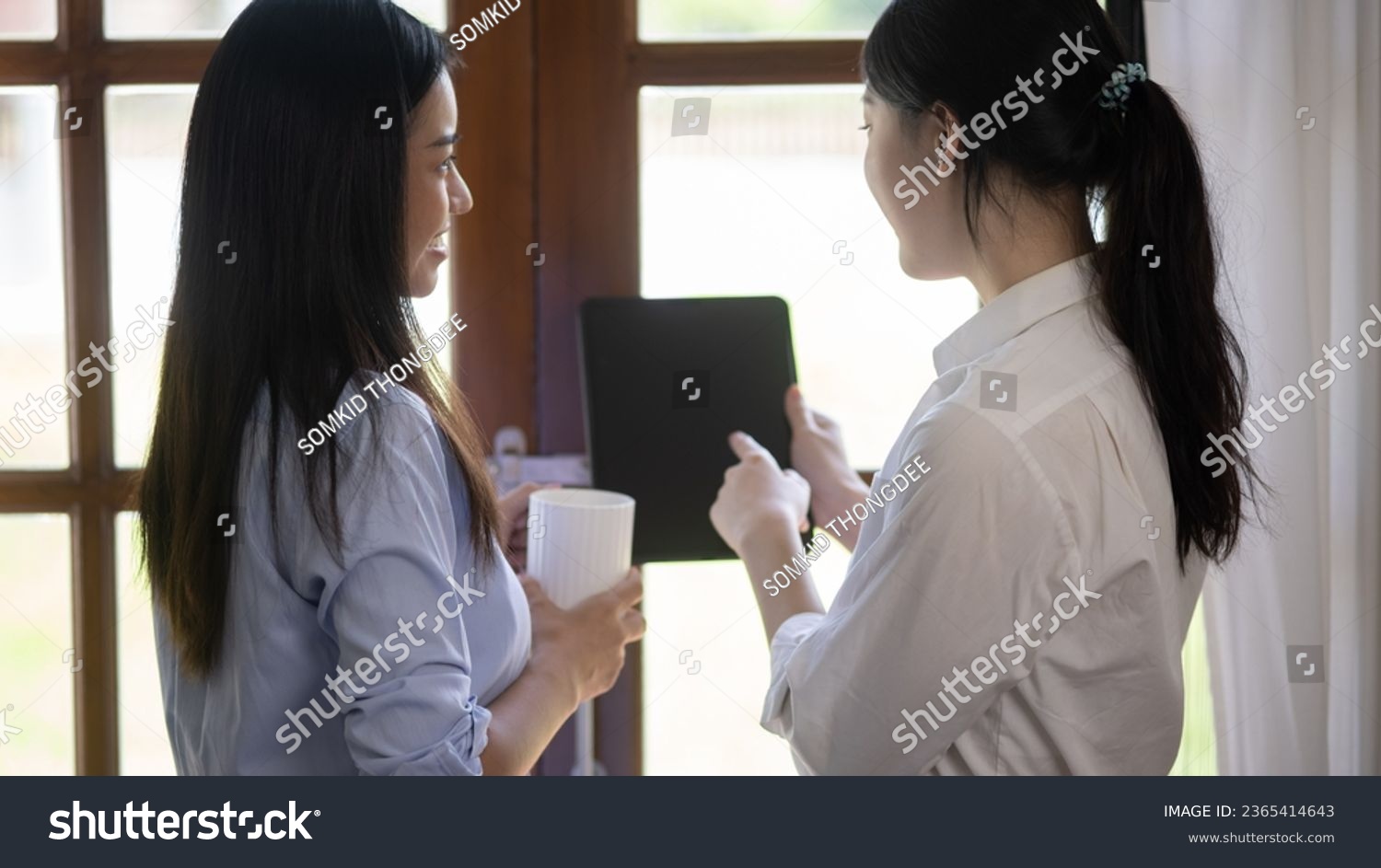 Two attractive Asian women holding a digital tablet and talking with friends at home, Two ideas woman. #2365414643