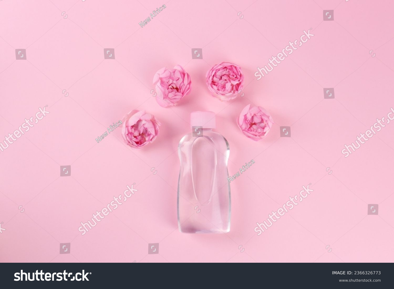 Bottle with baby oil and beautiful flowers on pink background, flat lay. Space for text #2366326773