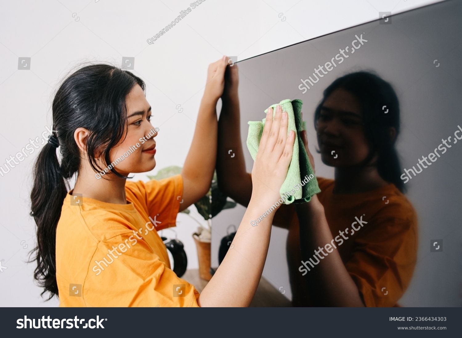 Young Asian woman cleaning tv screen with rag #2366434303