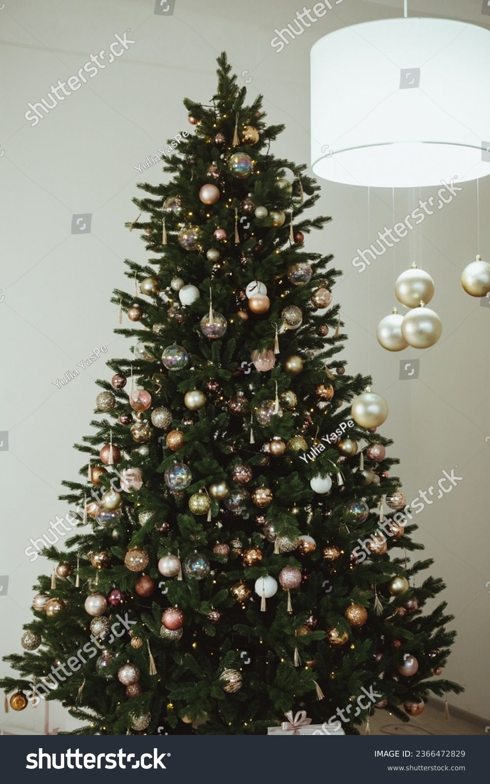 Big beautiful christmas tree decorated with beautiful shiny baubles and many different presents on wooden floor. White wall background with copy space. #2366472829