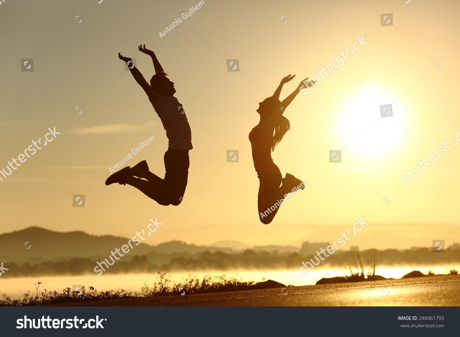 Fitness couple jumping happy at sunset with the sun in the background #246061795