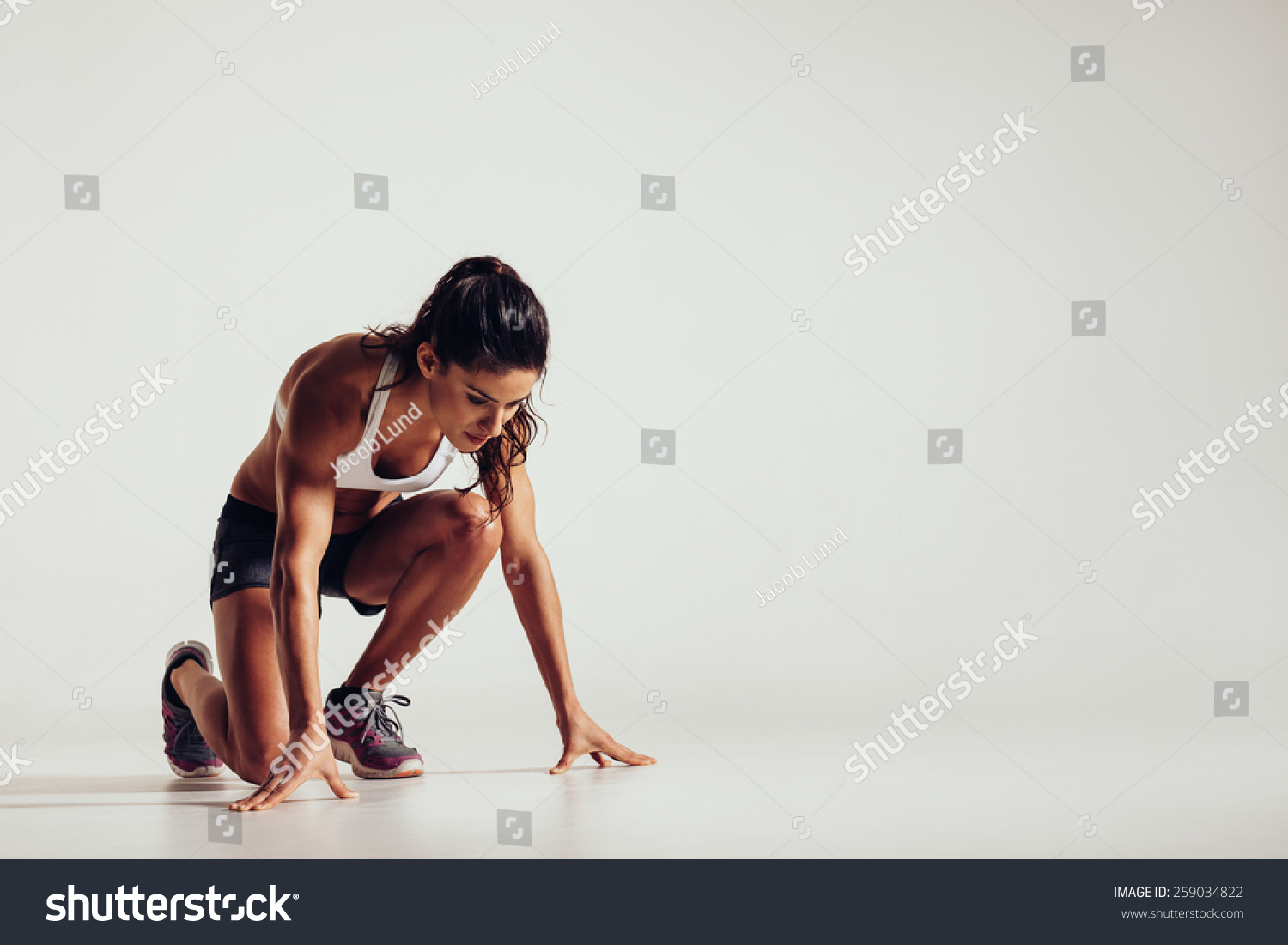 Healthy young woman preparing for a run. Fit female athlete ready for a spring over grey background with copy space. #259034822