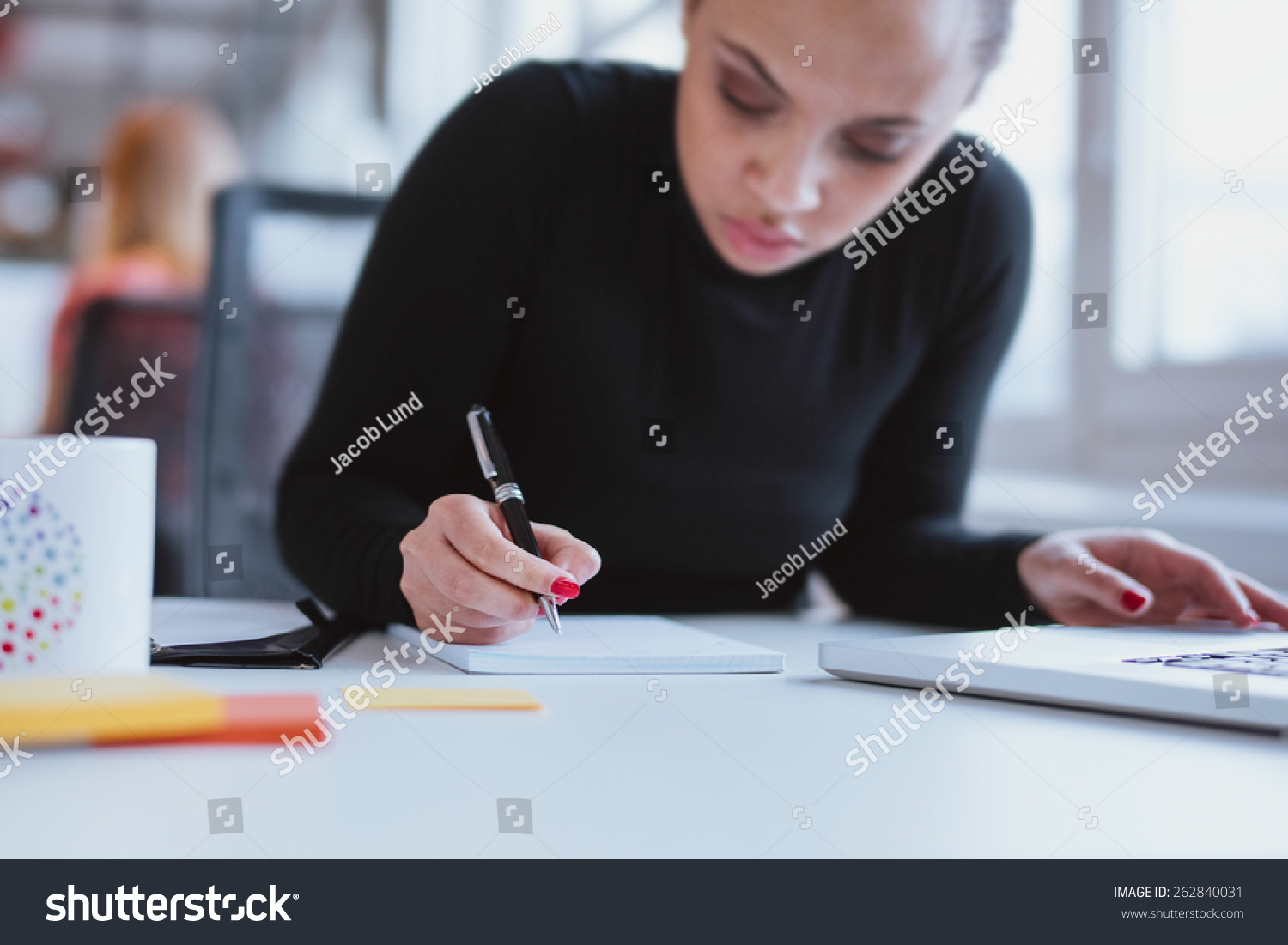 Young woman working at her desk taking notes. Focus on hand writing on a notepad. #262840031
