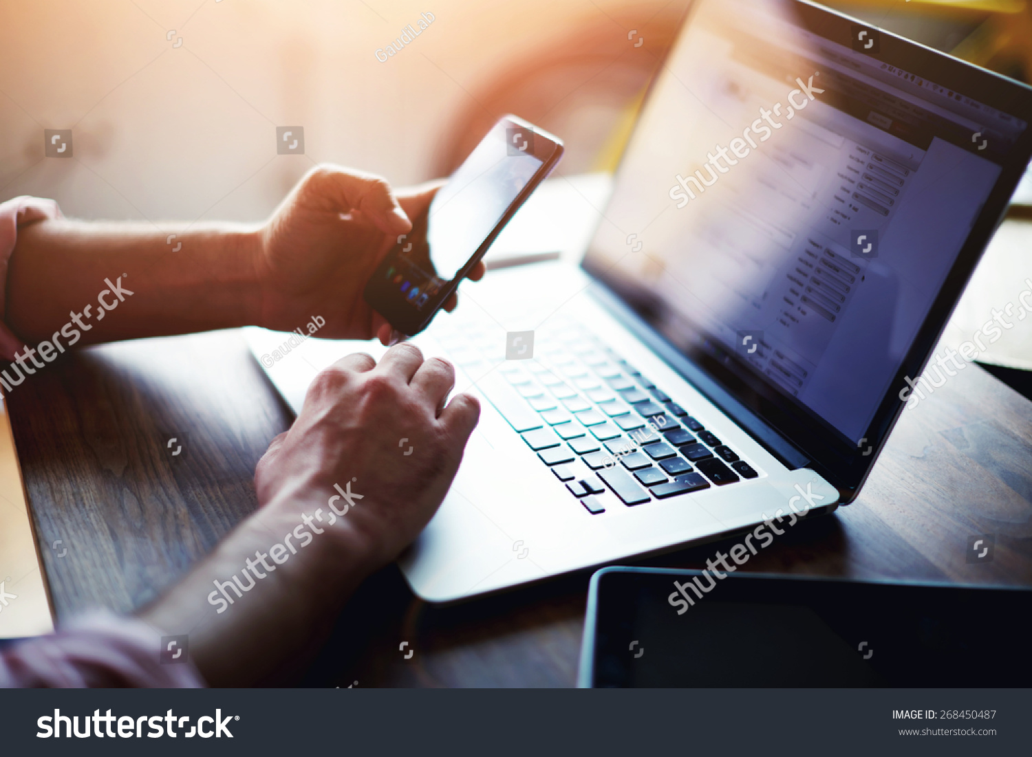 Side view shot of a man's hands using smart phone in interior, rear view of business man hands busy using cell phone at office desk, young male student typing on phone sitting at wooden table, flare #268450487