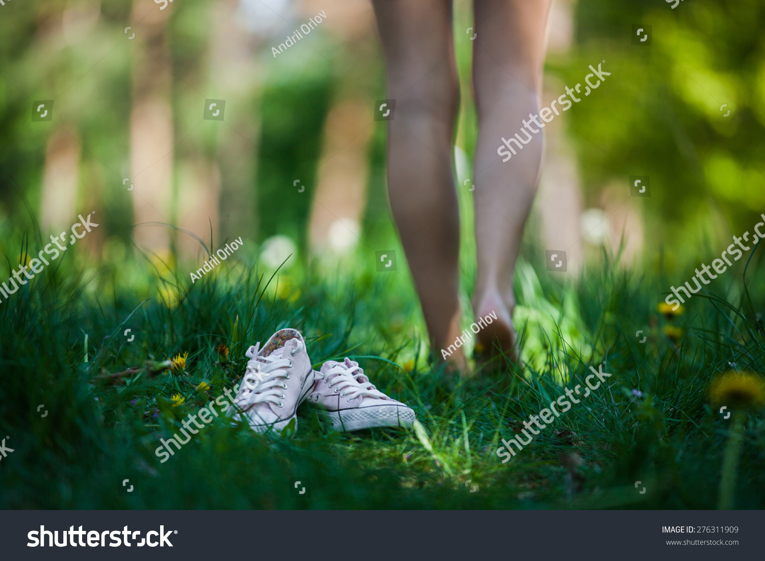 Woman walking barefoot on the green grass, shoes in focus, shallow DOF #276311909