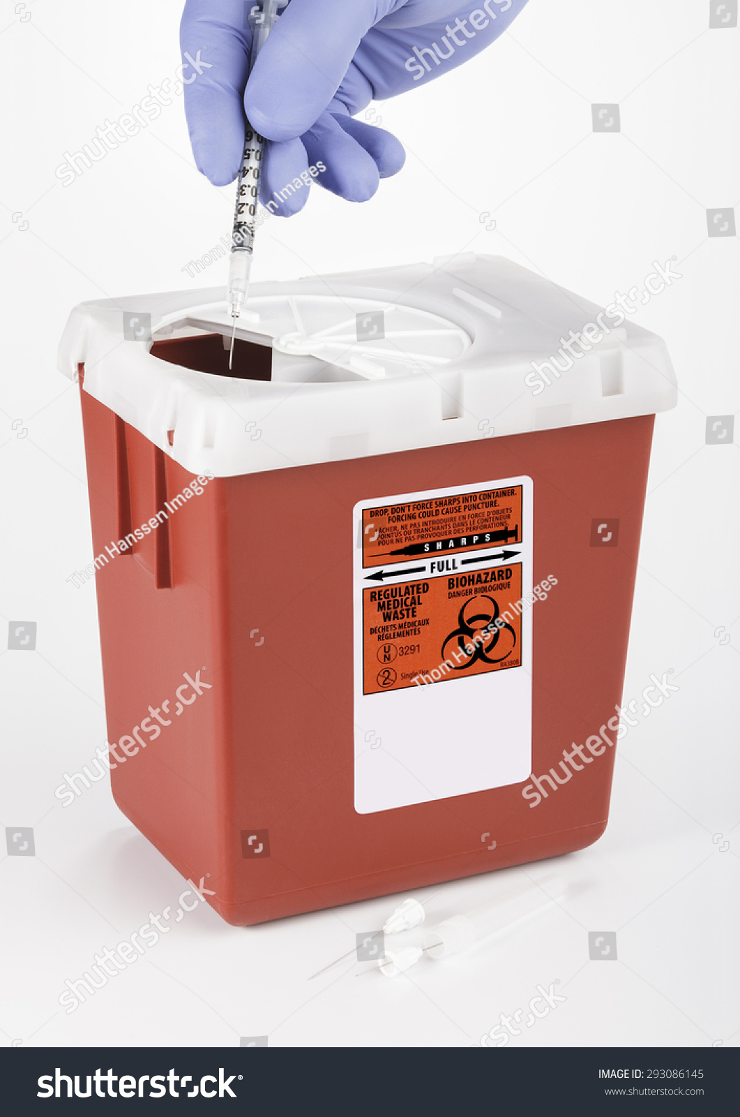 A gloved hand inserting Medical and/or Dental waste into a medium size Sharps container. White background. #293086145