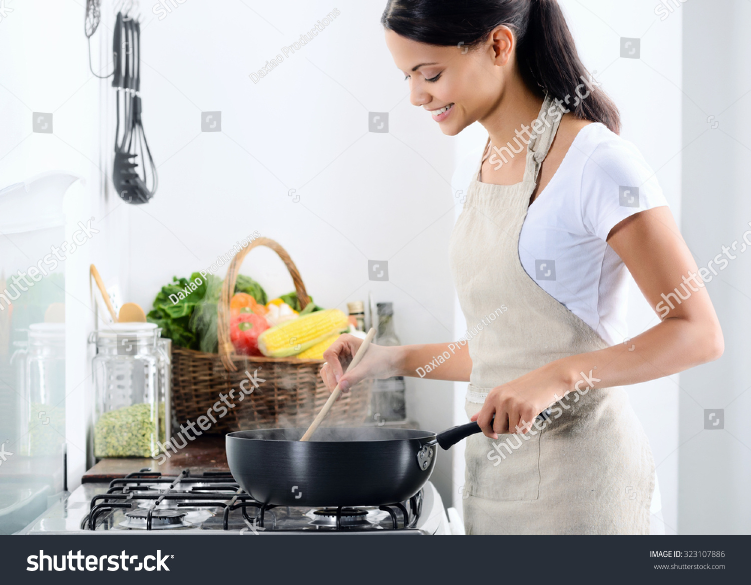 Woman standing by the stove in the kitchen, cooking and smelling the nice aromas from her meal in a pot #323107886