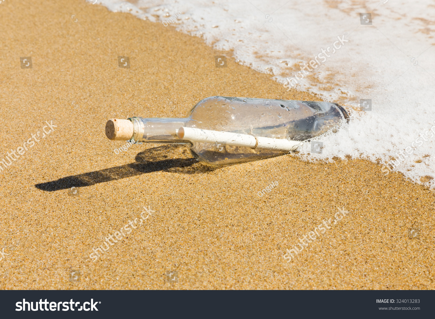 Message in a bottle washed up by the sea lying half submerged in the golden beach sand on the edge of the surf in a conceptual image of romance or a shipwreck. #324013283