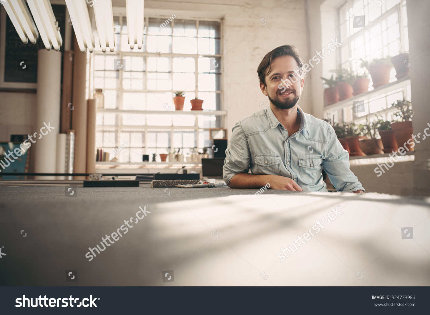 Portrait of a small business owner sitting casually in his worskhop studio looking confident and positive #324738986