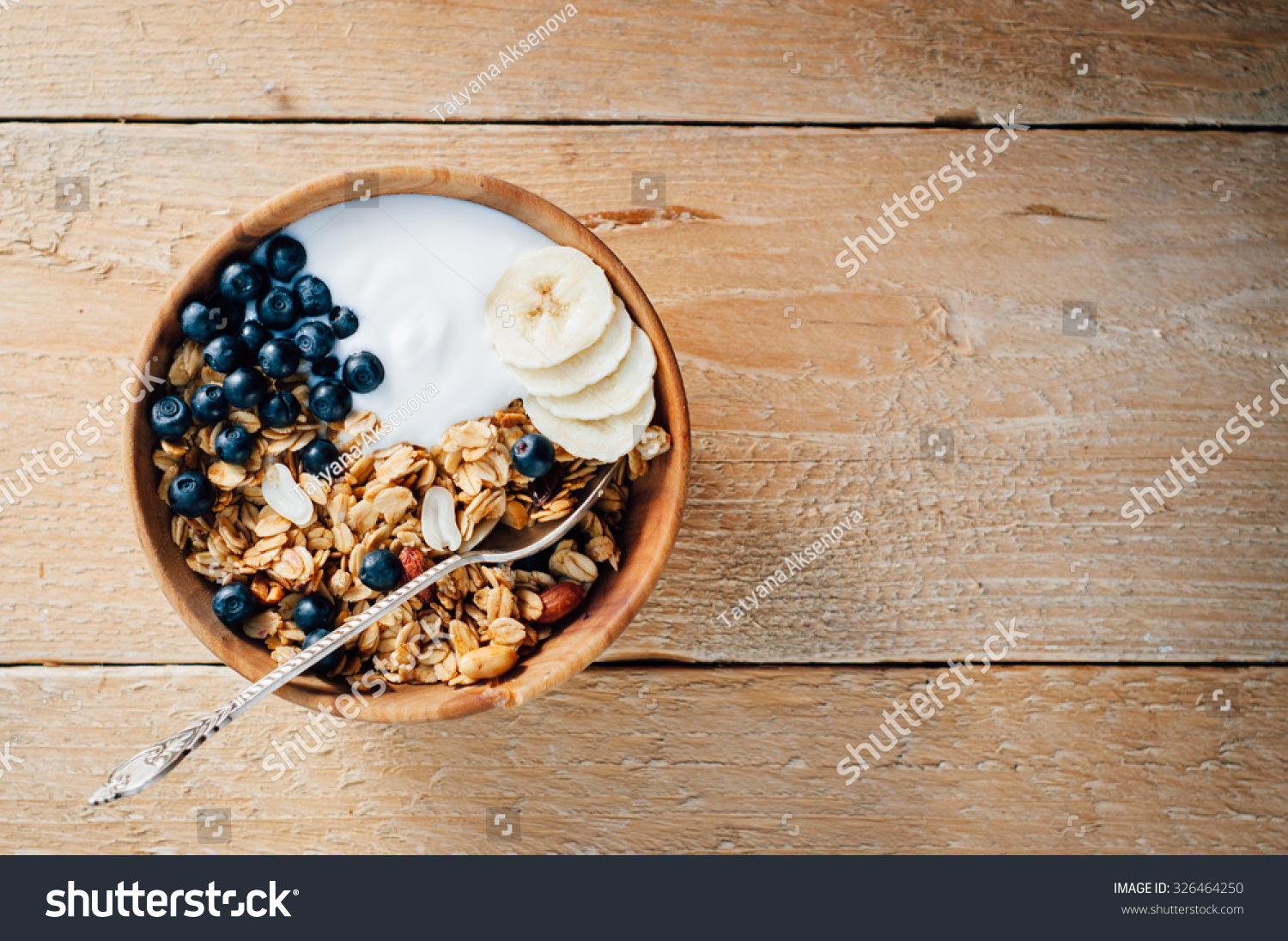 Homemade oatmeal granola with peanuts, blueberry and banana in wooden bowl, sunny morning #326464250