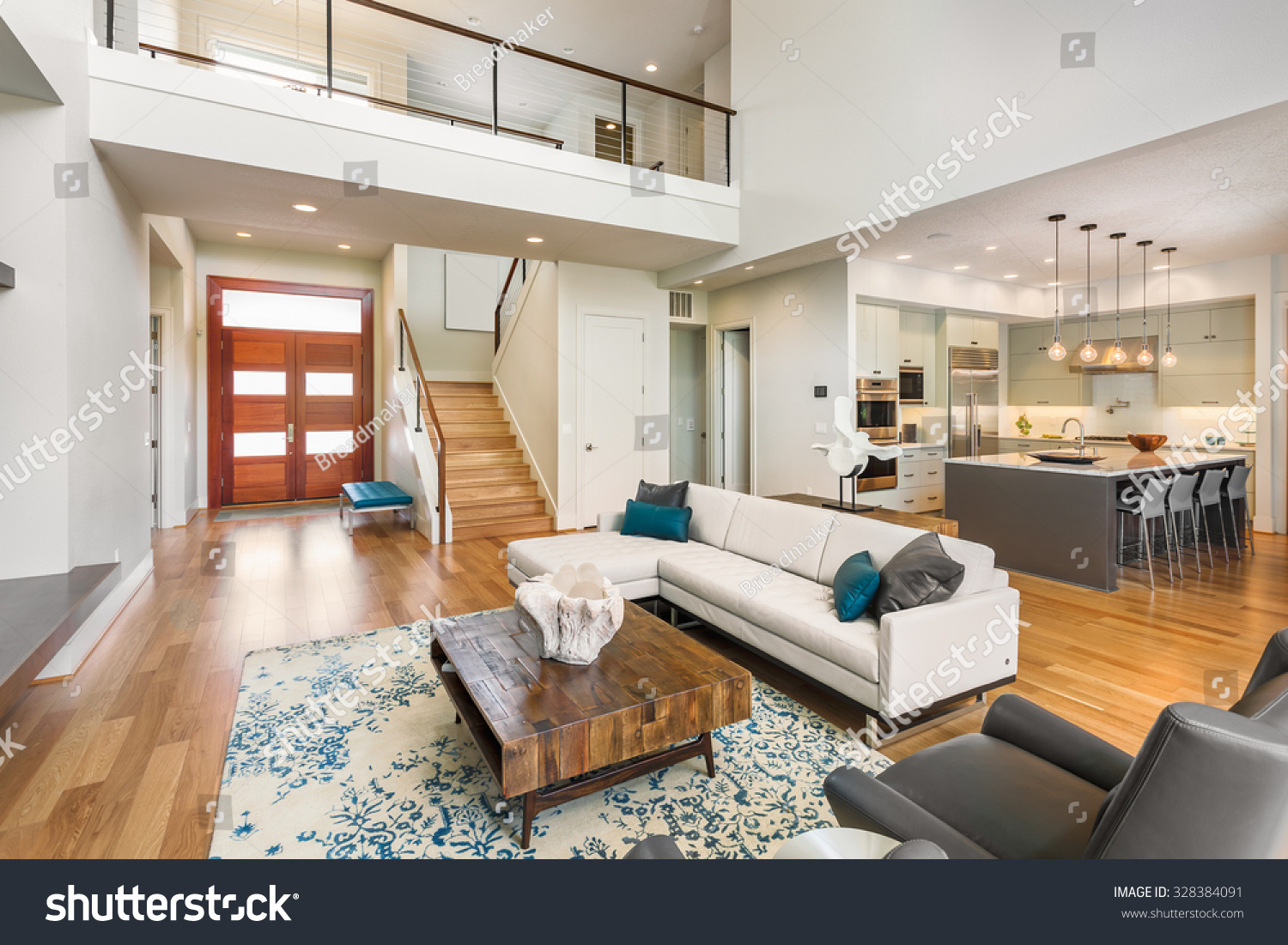 Beautiful and large living room interior with hardwood floors and vaulted ceiling in new luxury home. View of Kitchen, entryway, and second story loft style area #328384091
