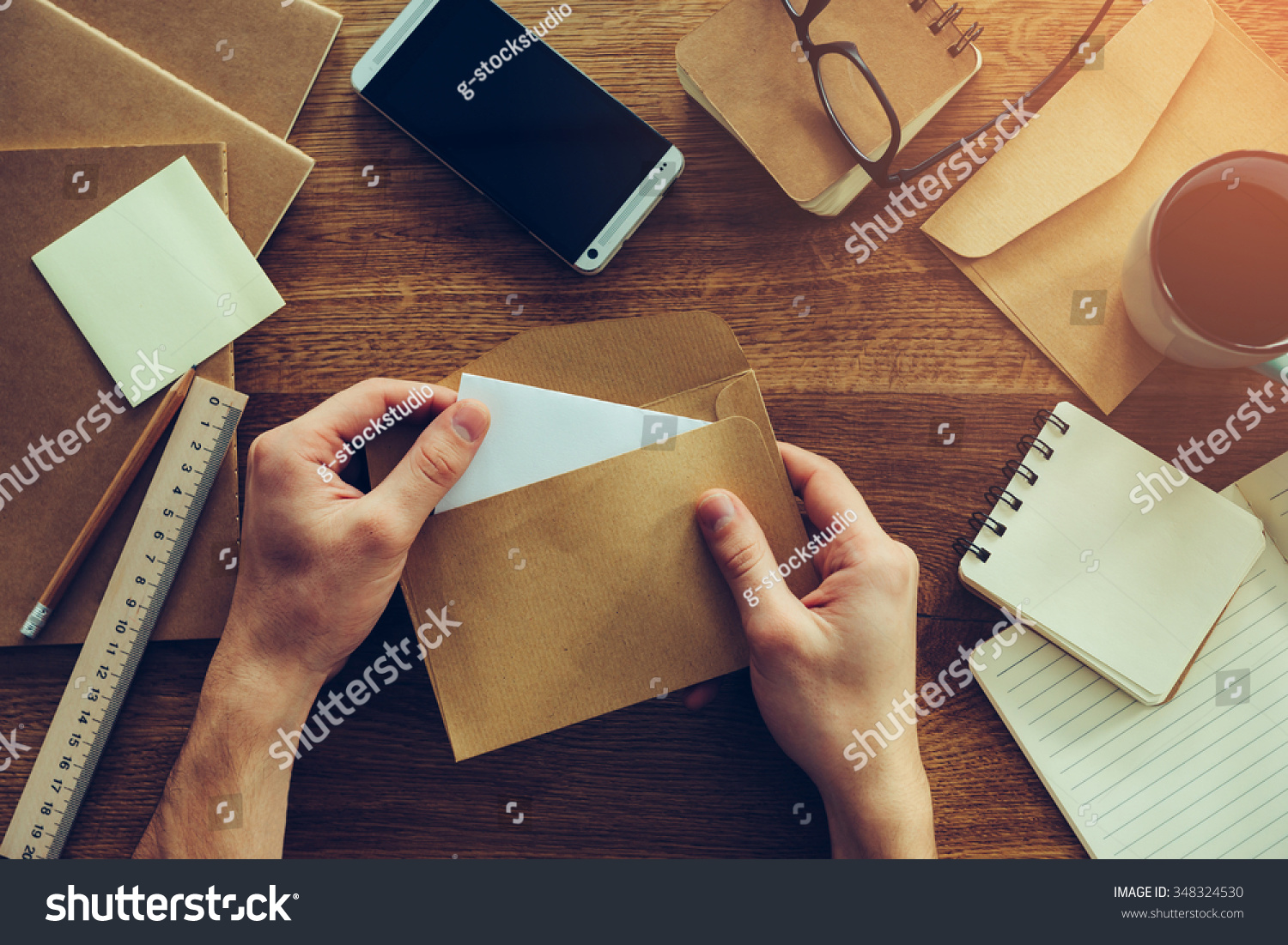 Opening envelope. Close-up top view of male hands opening envelope over wooden desk with different chancellery stuff laying on it #348324530