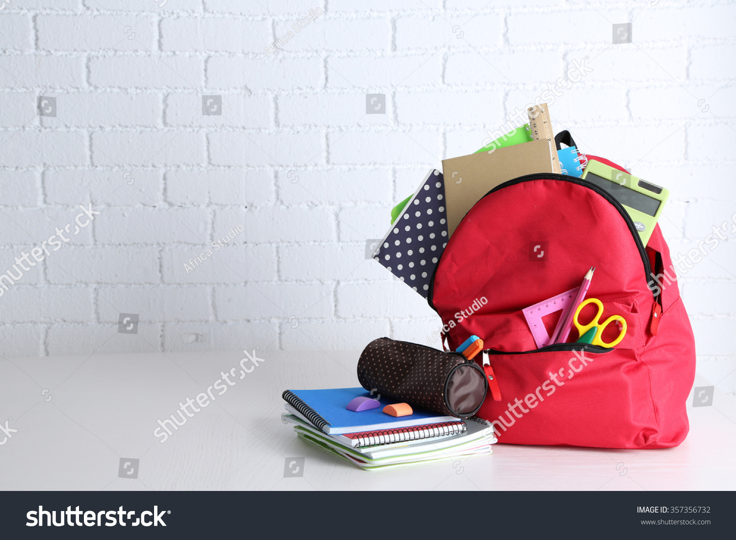 Backpack with school supplies on wooden table, on wall background #357356732
