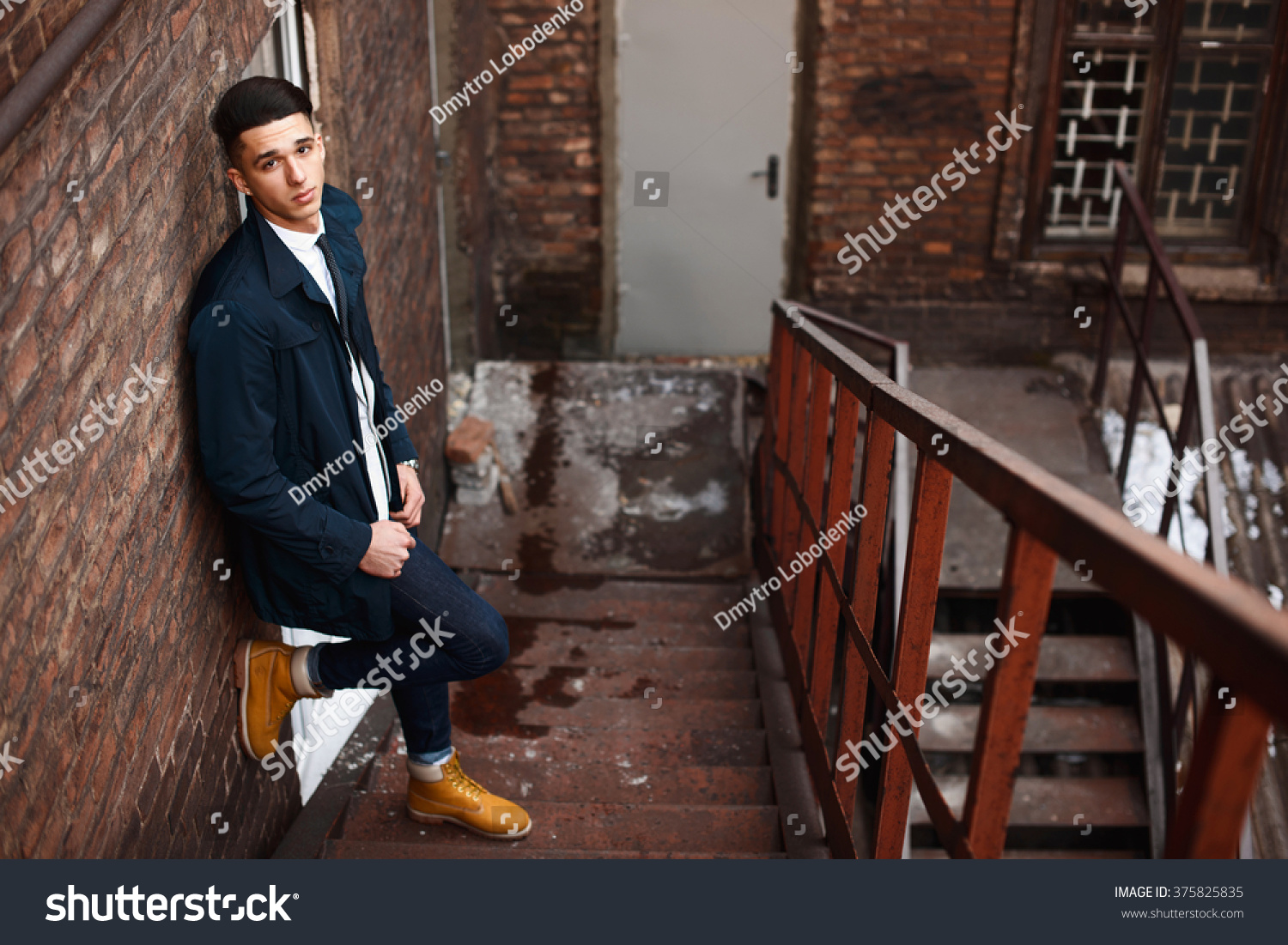 Young hipster man on stairs. A man wearing in a blue jacket , a white shirt, blue jeans and yellow boots #375825835