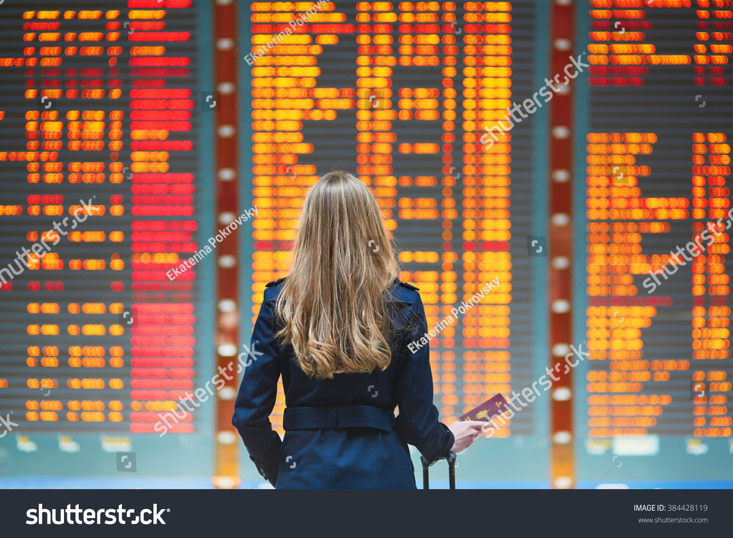 Young woman in international airport looking at the flight information board, checking her flight #384428119