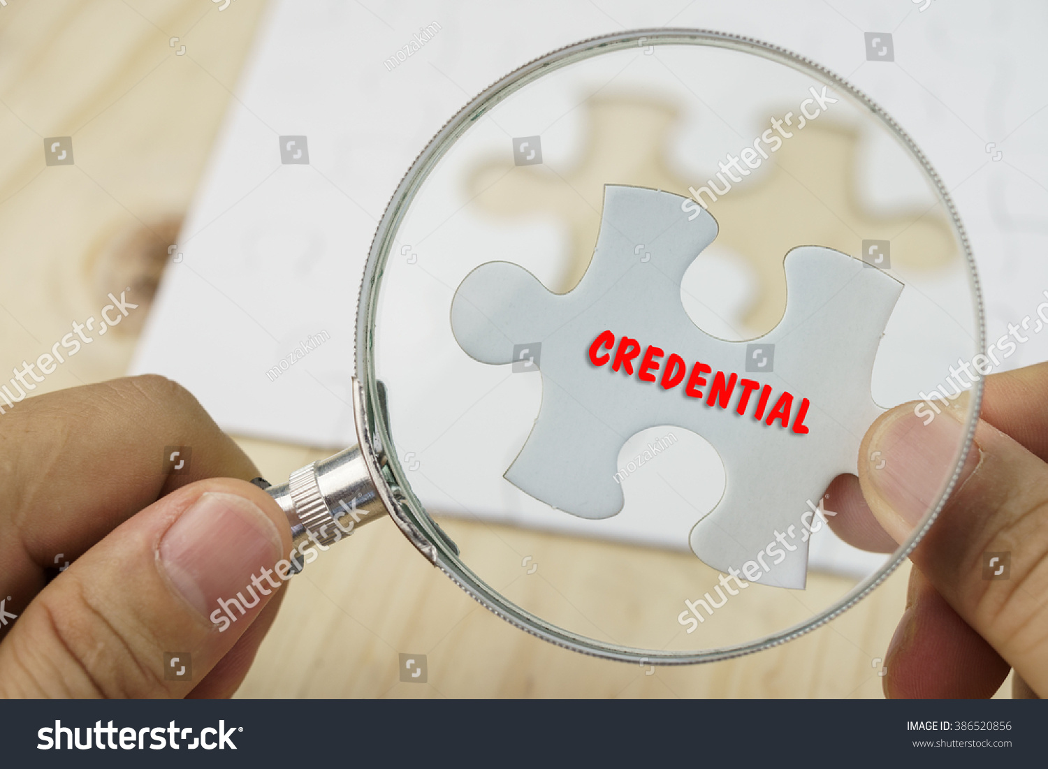 Business concept.Hand with magnifying glass searching for a piece of jigsaw puzzle with CREDENTIAL word. #386520856